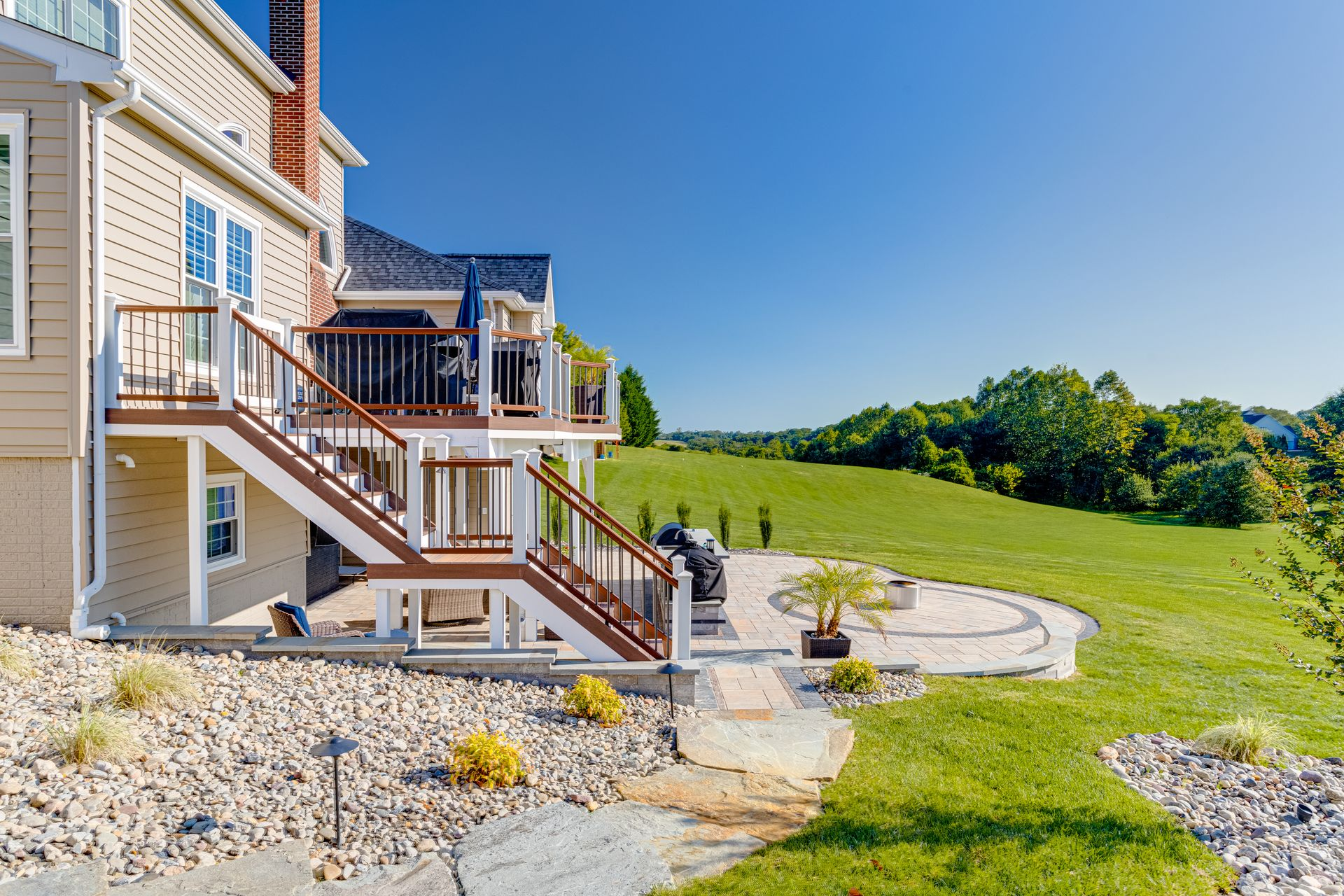 Backyard patio and stairs beside a house, overlooking a grassy lawn under a clear blue sky