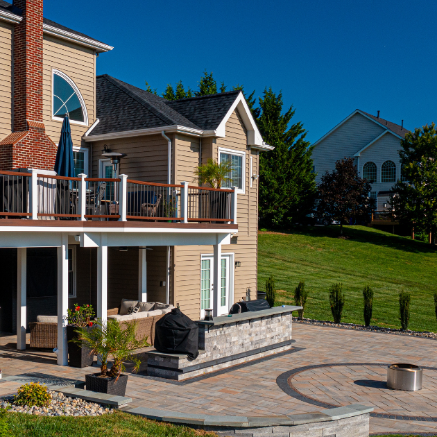 Custom backyard patio and multi-level deck with stone wall and lawn, designed by Xscape 2 Nature in Maryland.