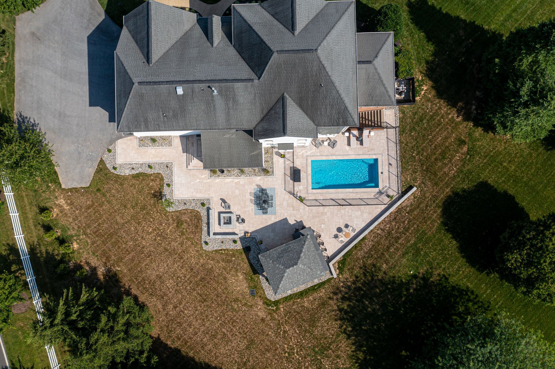 Backyard patio with raised wooden deck, concrete floor, and black pergola beside a house