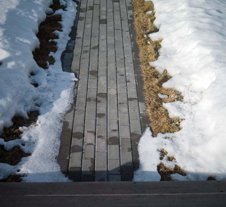 Brick pathway flanked by snow melting on patches of brown grass.