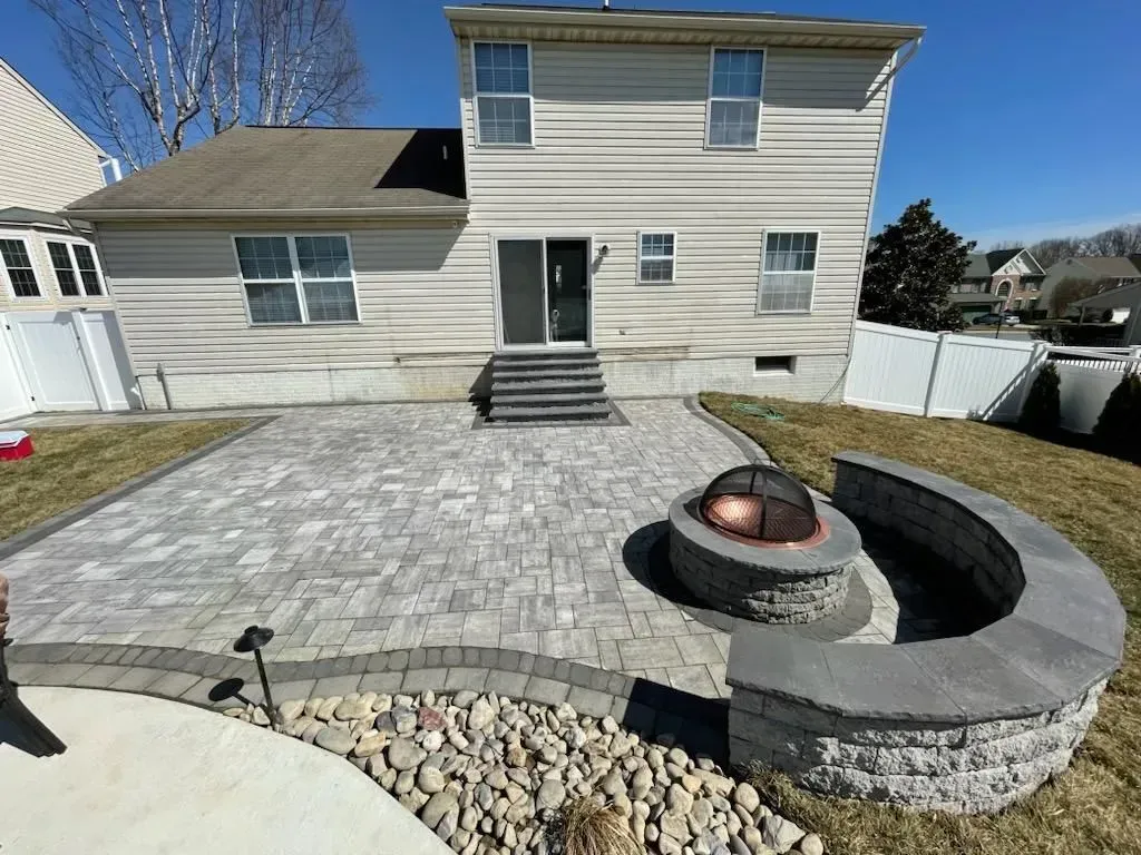 Backyard patio with fire pit, pavers, and house with sliding glass door.