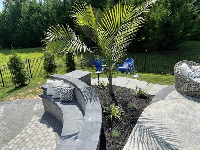 Outdoor patio with built-in seating, flower bed with a palm tree and ferns against a green background.