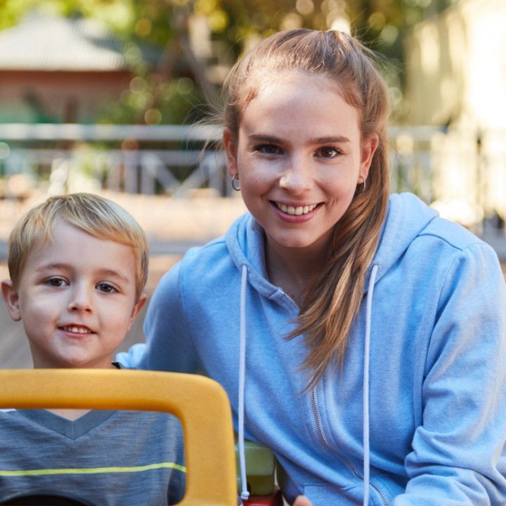 A woman is sitting next to a young boy in a yellow toy car