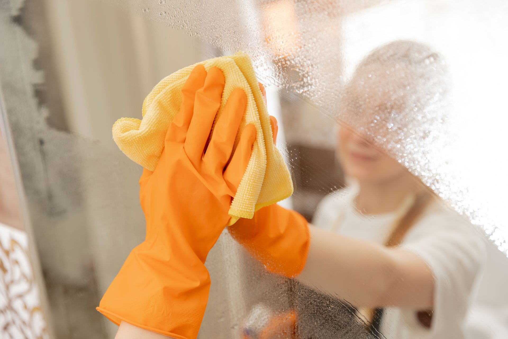 A person wearing orange gloves is cleaning a window with a cloth.