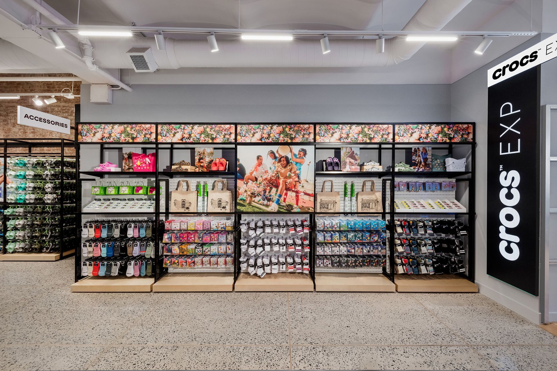 Crocs store interior. Display shelves stocked with shoes, Jibbitz, and accessories. Neutral colors, modern design.