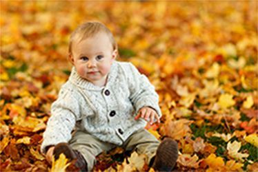 A baby is sitting in a pile of leaves.