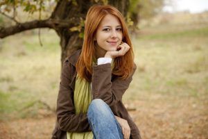 A woman with red hair is sitting under a tree.