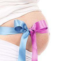 A pregnant woman is tied with a blue and pink ribbon.
