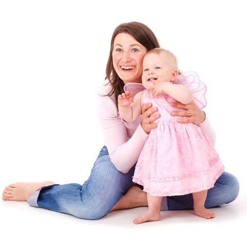 A woman is kneeling down holding a baby in a pink dress
