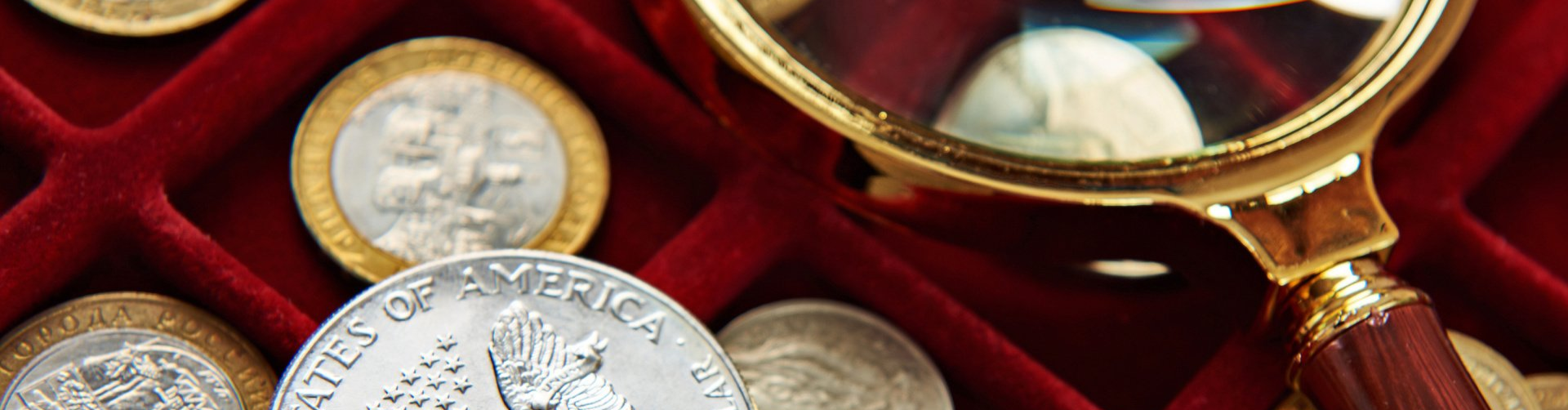 collectible coins in a red velvet box with a magnifying glass laying nearby