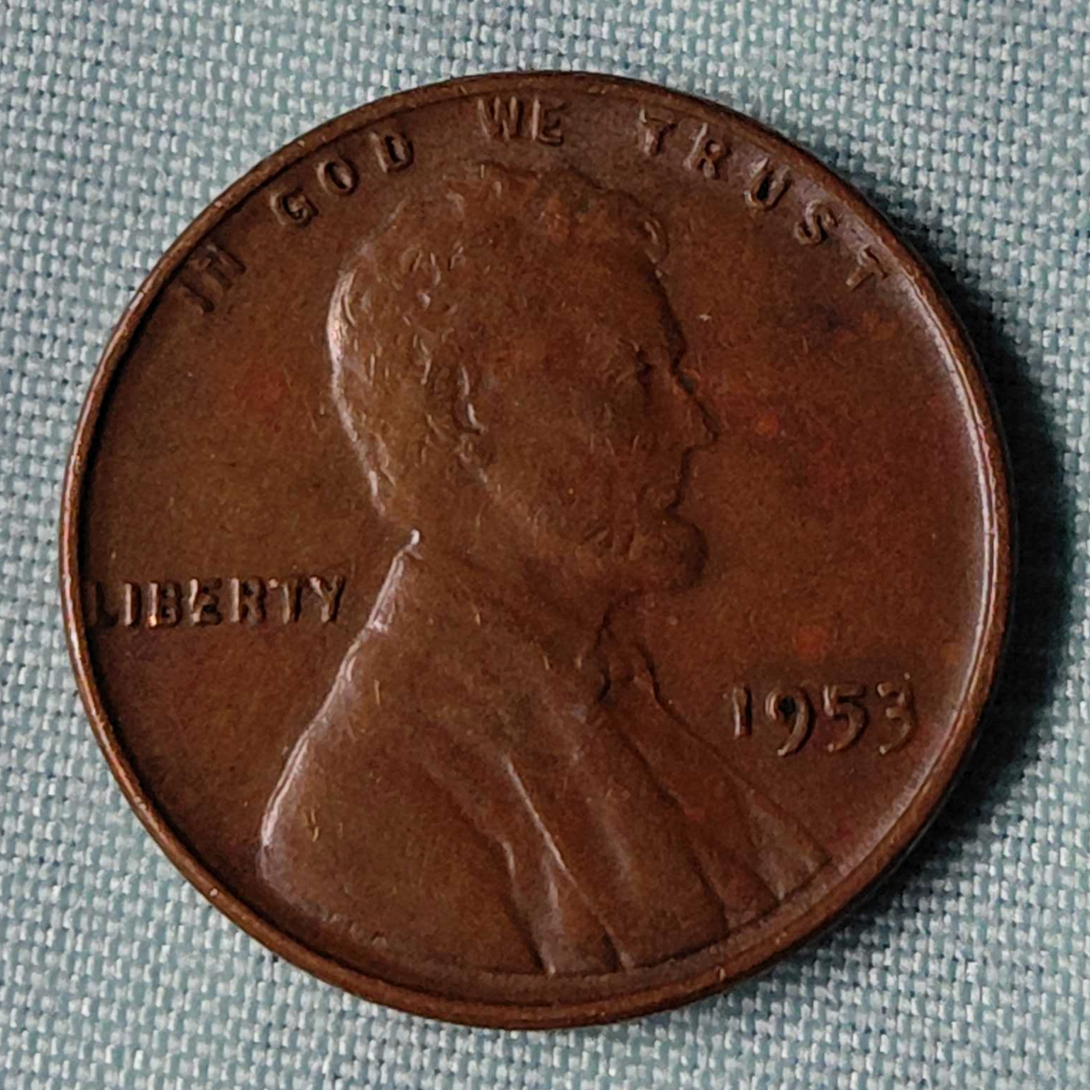 Close-up of a worn 1953 Lincoln wheat penny on a gray fabric background