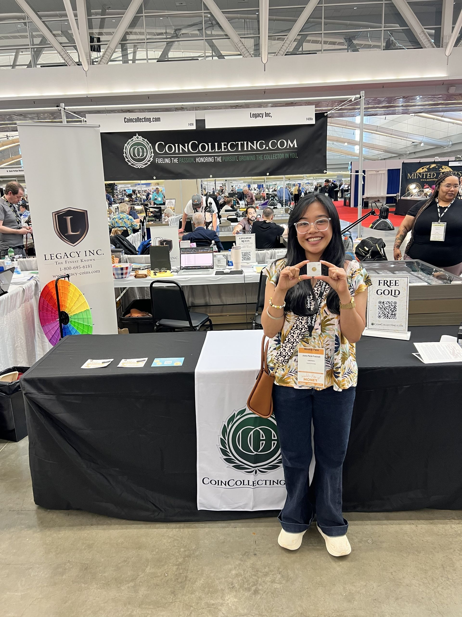 Woman smiling and holding a phone at a trade show booth with black banners and display tables