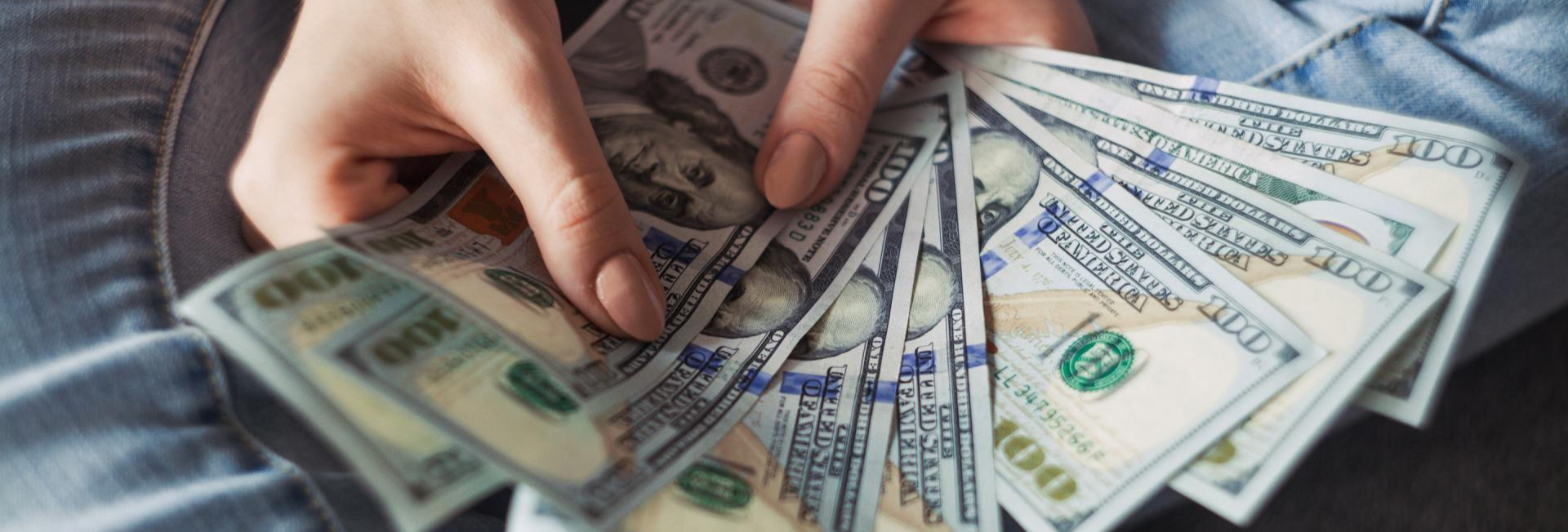 person holding fanned out 100 dollar bills