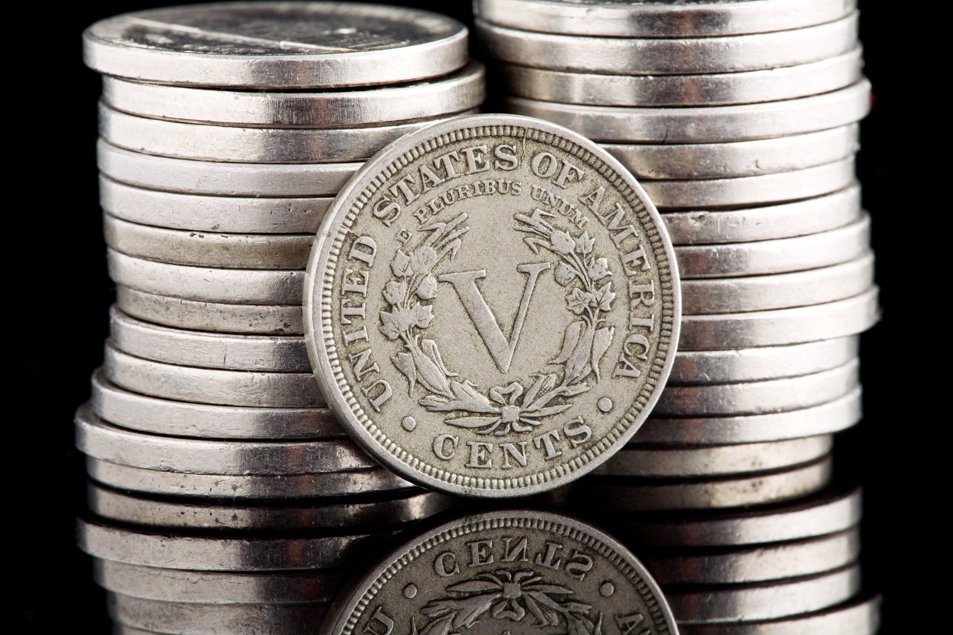 Liberty head v nickel leaning against a stack of nickels on a shiny black background