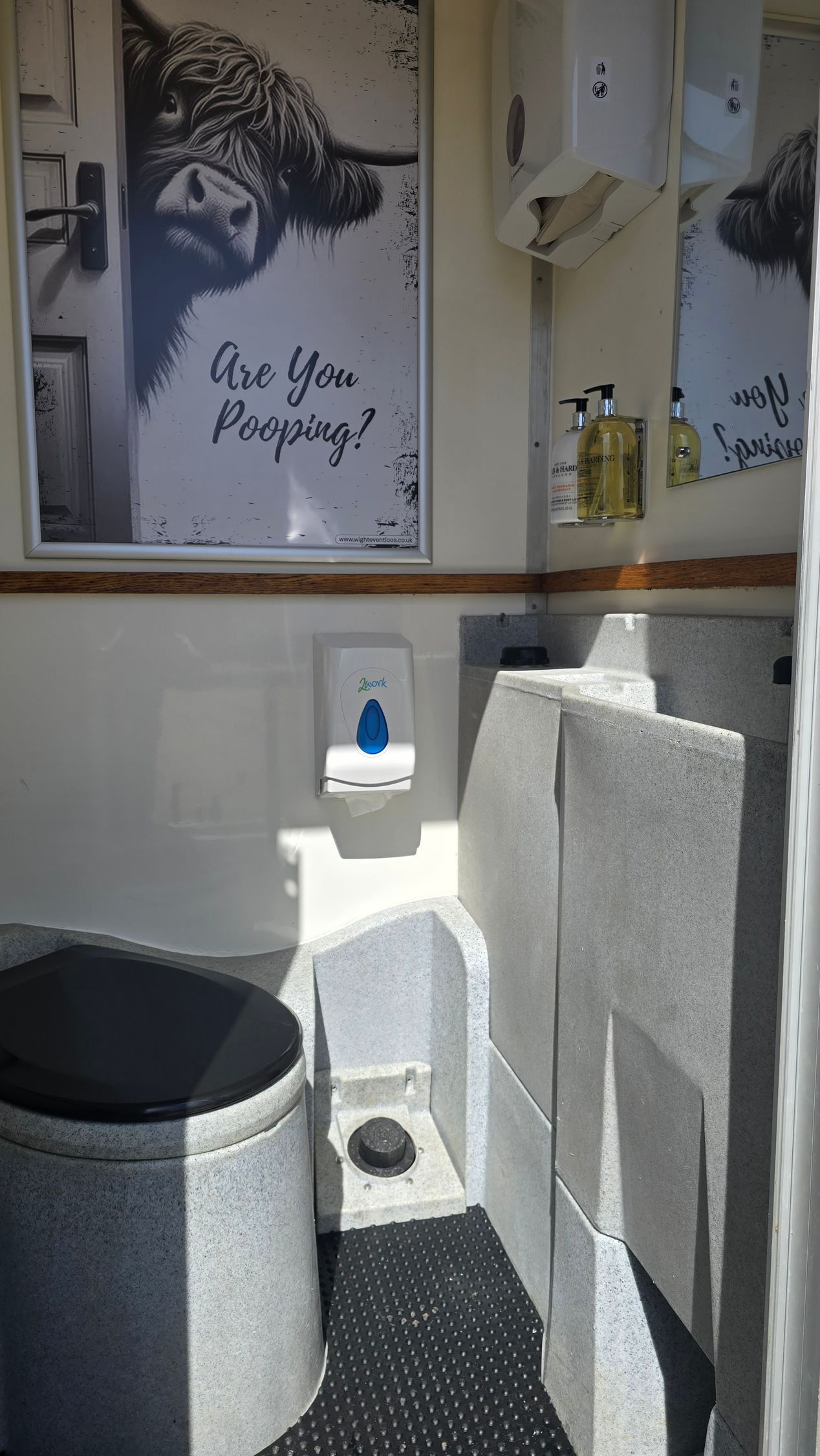 Small restroom with a toilet, sink, and gray tiled walls under a framed cow poster.