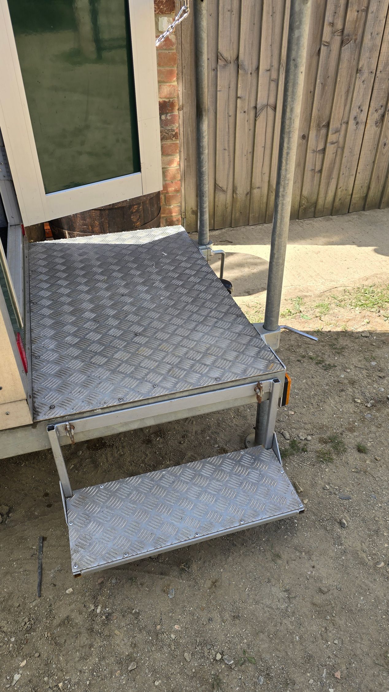 Metal stairs and platform beside a door, with a small lower step over gravel.