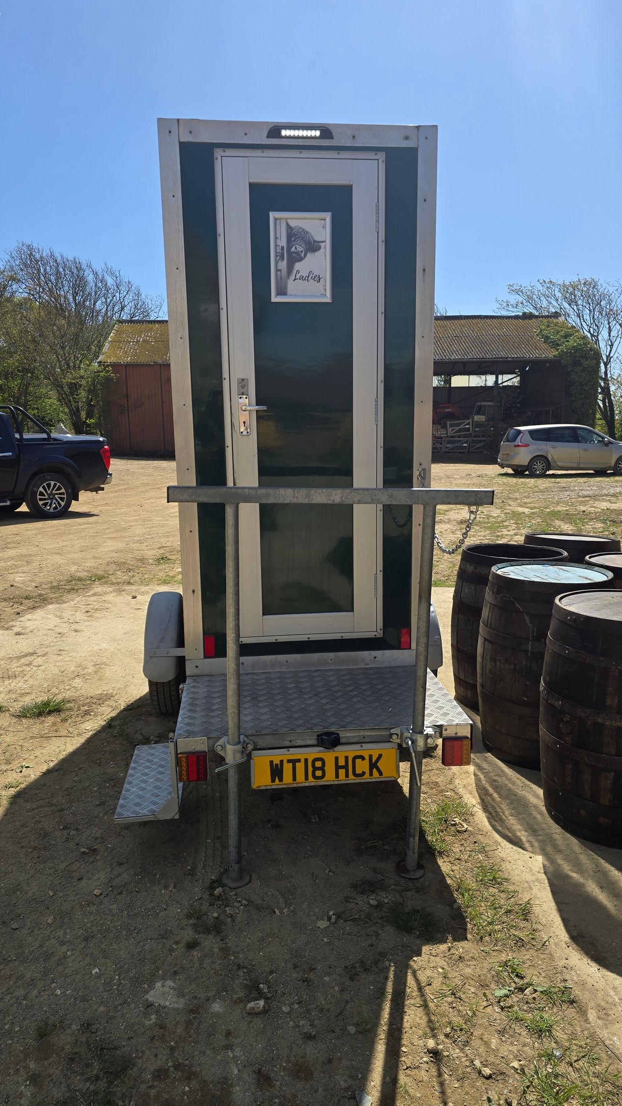 Rear view of a small utility trailer with a green cabinet, parked on grass under a blue sky.