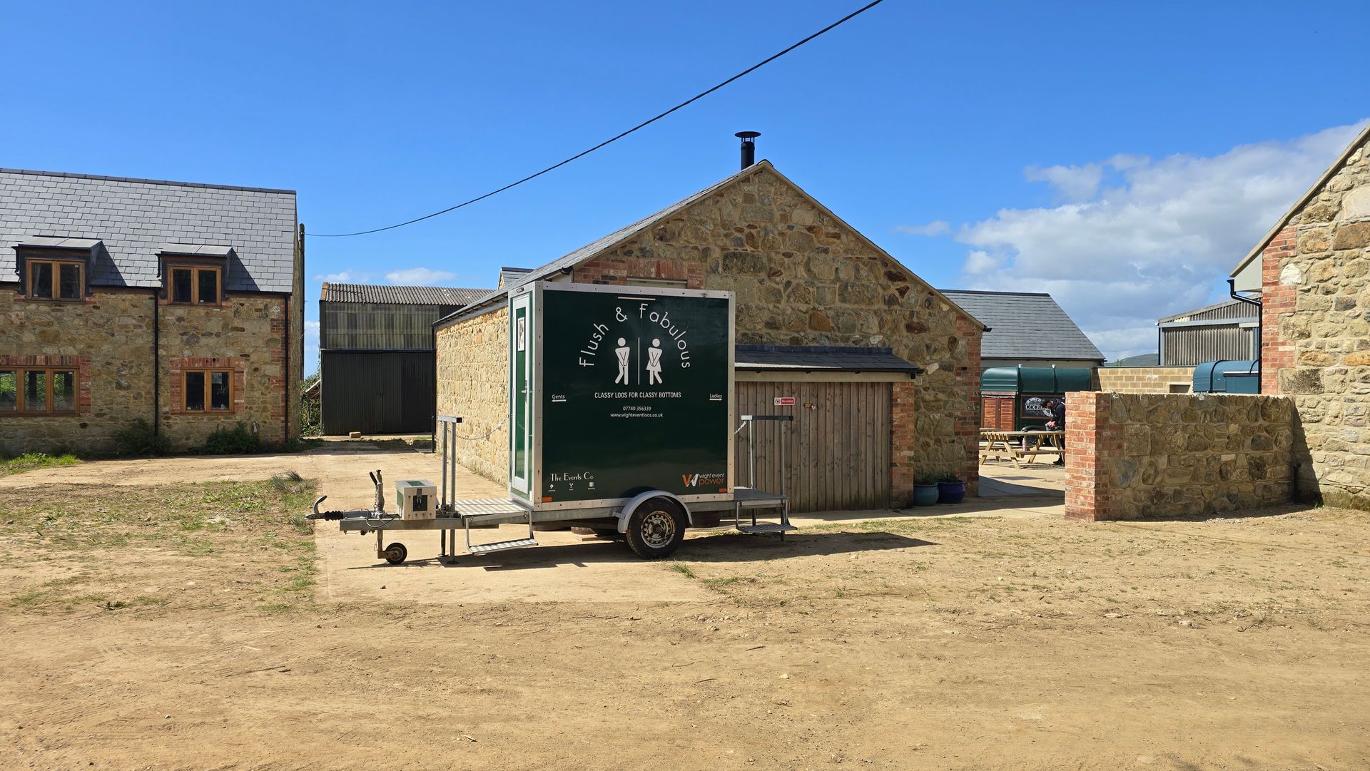 Trailer beside a stone building in a sunny rural yard, with a blue sky overhead.