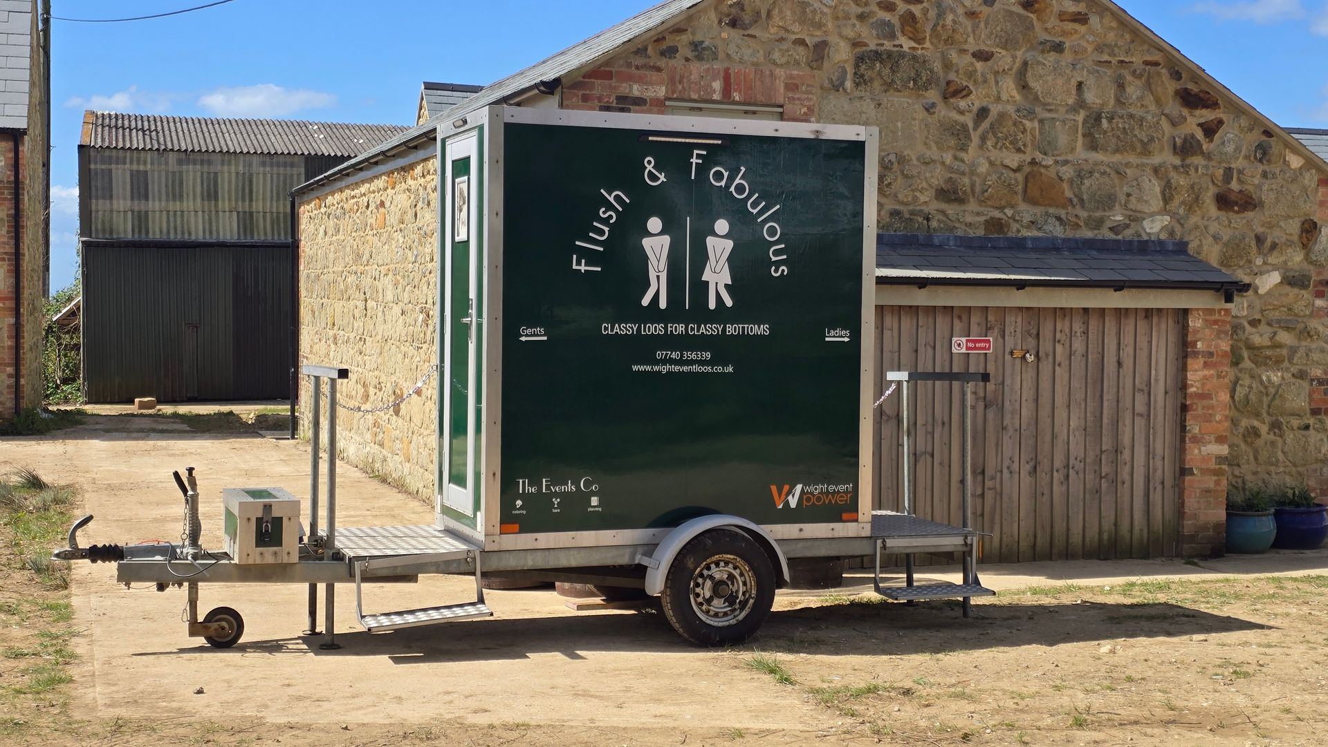 Green food-trailer parked beside a stone building under a clear blue sky.