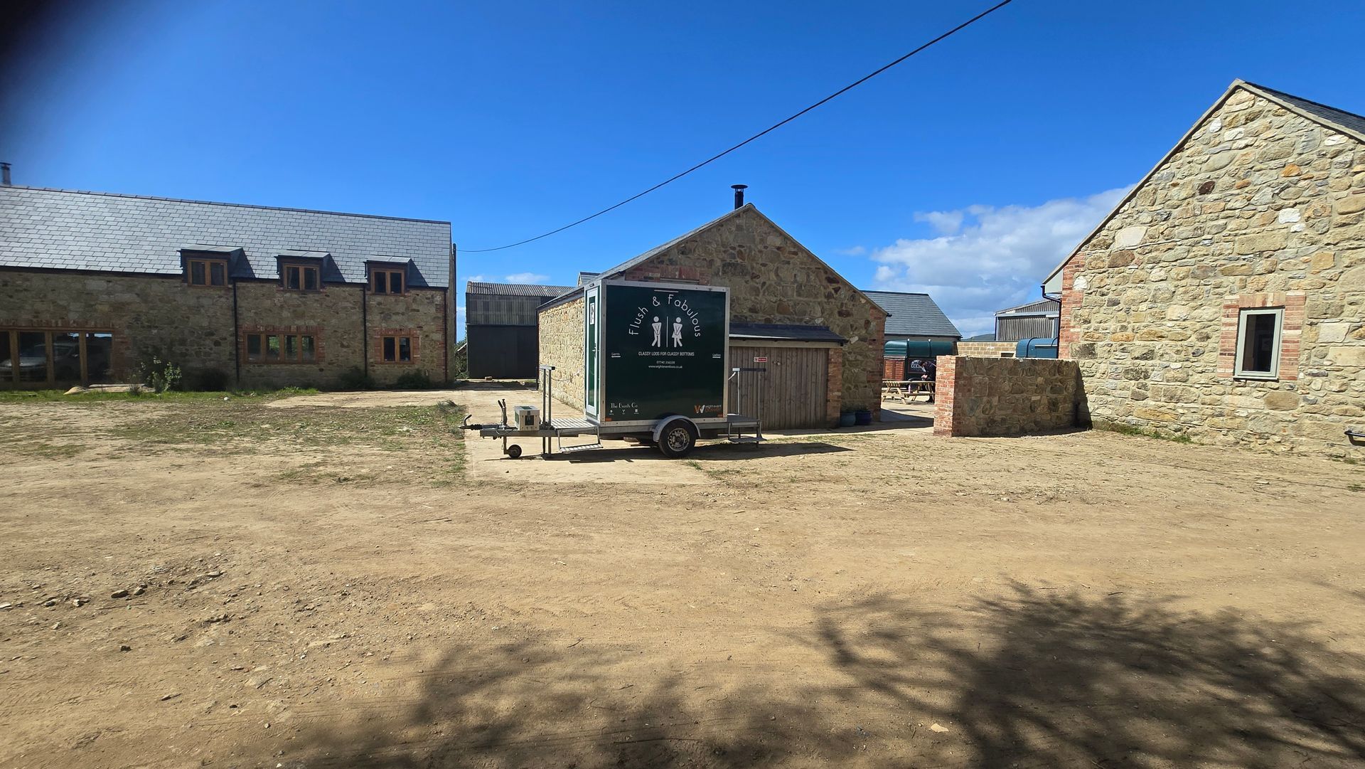 Stone buildings and a trailer in a sunny dirt courtyard under a blue sky