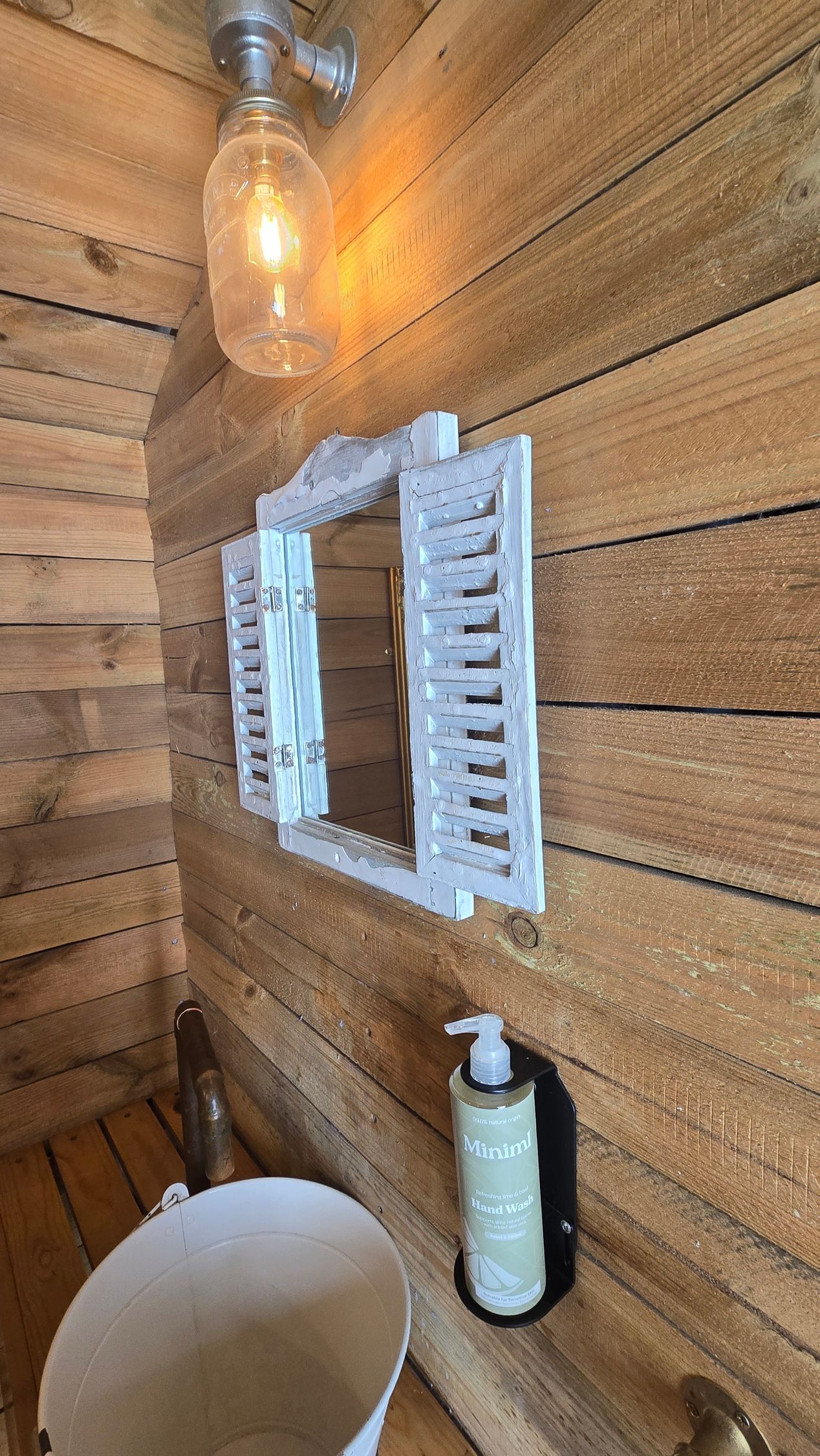 Rustic wooden bathroom wall with lit bulb, white mirror cabinet, sink basin, and soap dispenser.