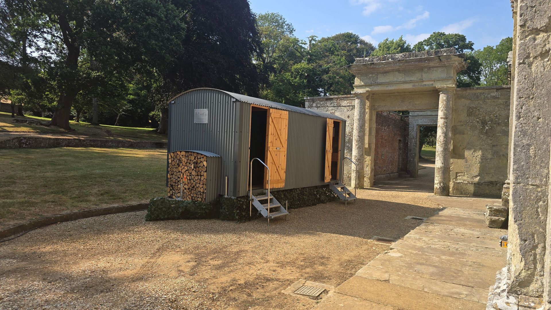 Small utility trailer beside a stone gate and wall in a sunny outdoor courtyard