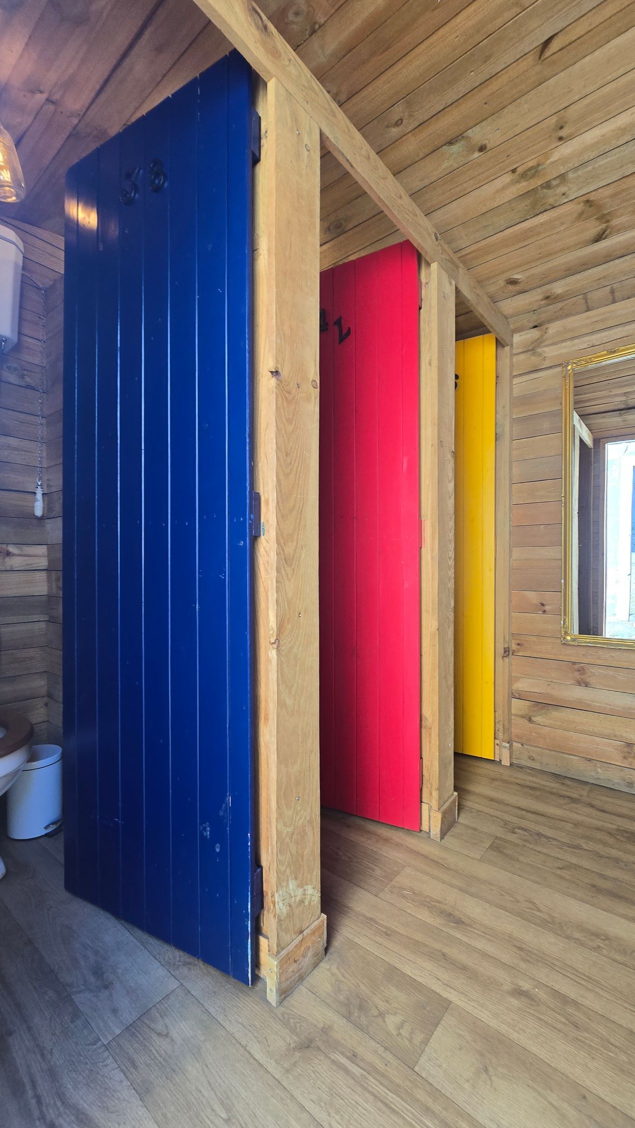 Colorful doors in a wooden hallway: blue, pink, and yellow stalls under a sloped wood ceiling.