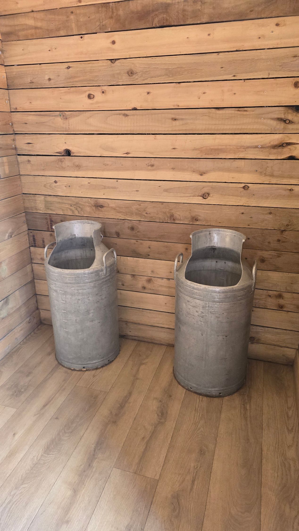 Two gray cylindrical planters on a wood floor against a wooden slat wall.