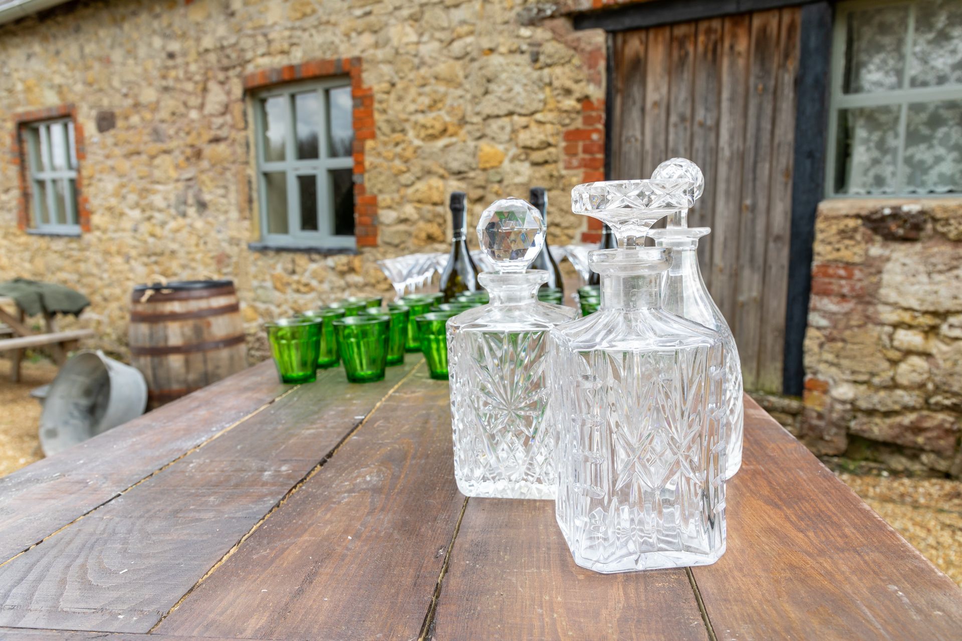 A wooden table with bottles and glasses on it in front of a stone building.