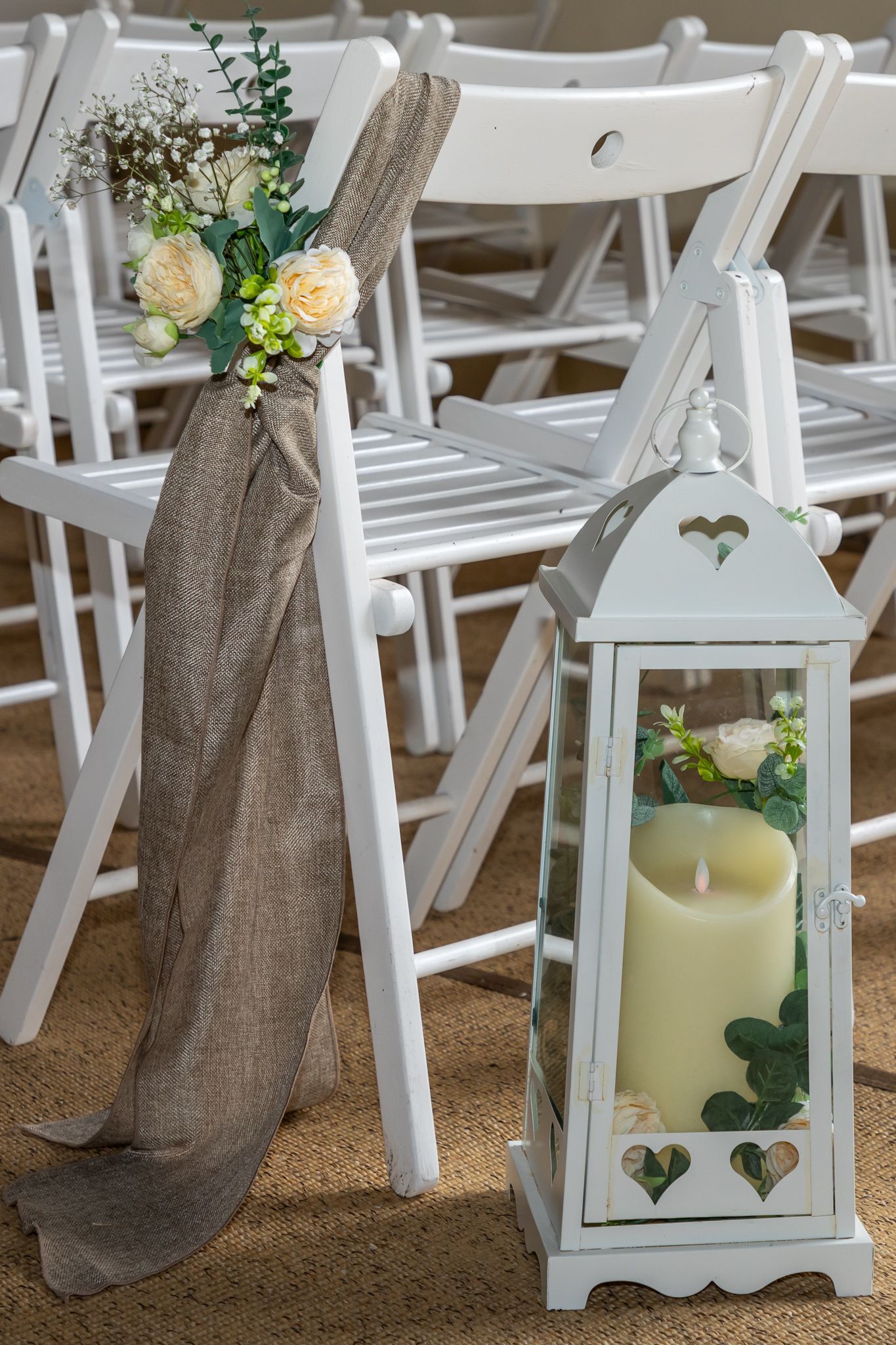 A white lantern with a candle inside of it is sitting next to a row of white folding chairs.