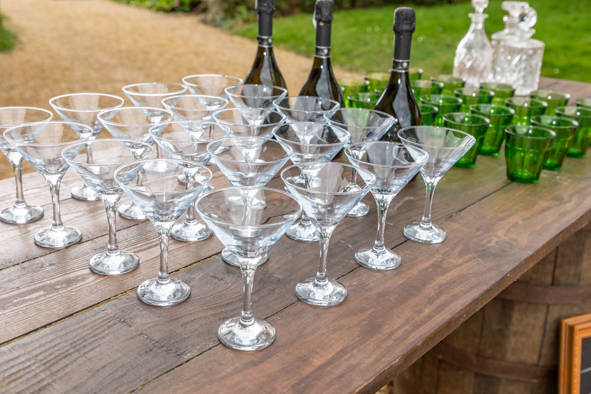 A wooden table topped with lots of martini glasses and bottles of wine.