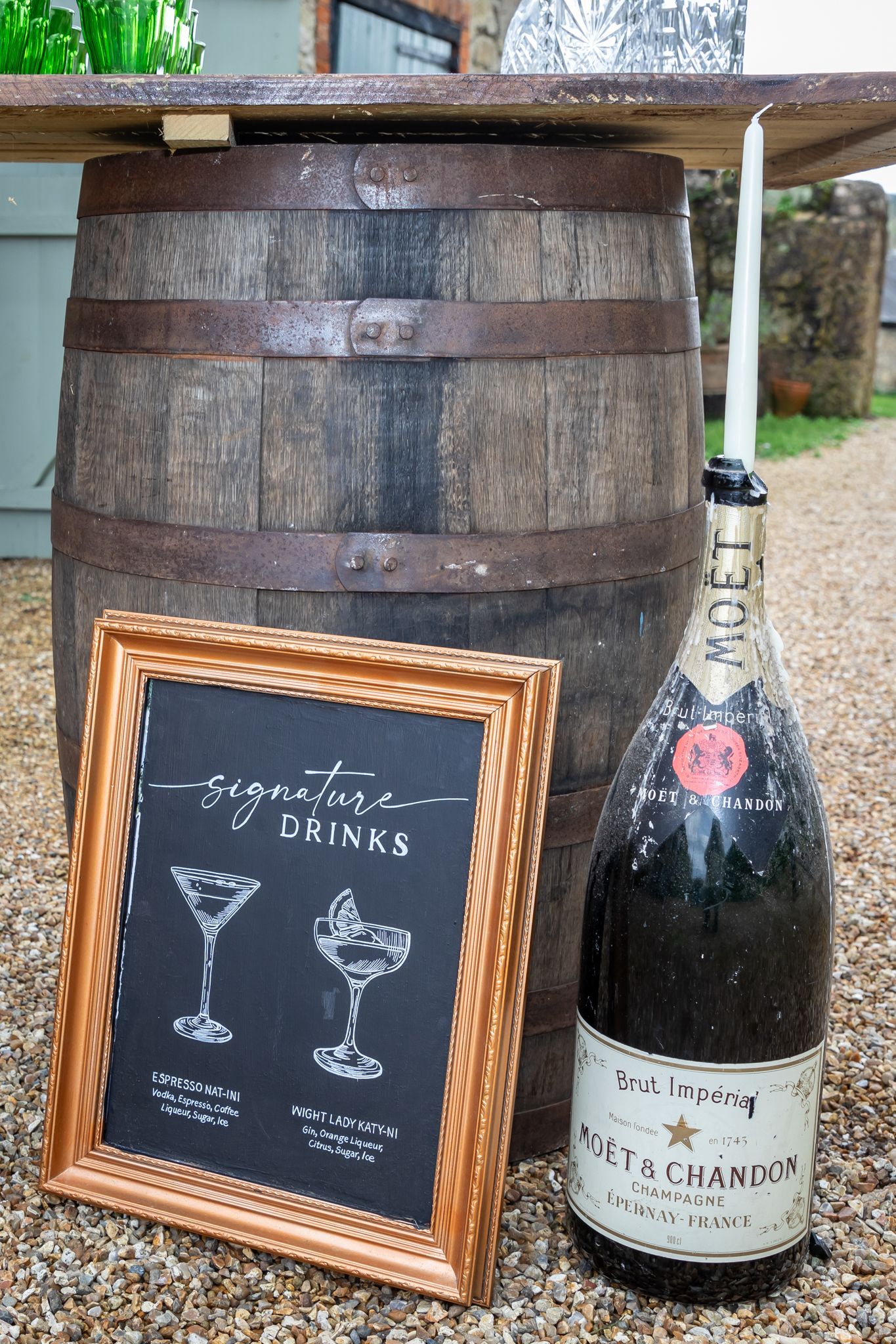 A bottle of champagne is sitting next to a barrel and a chalkboard.