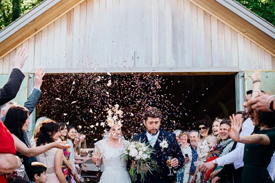 A bride and groom are being showered with confetti by their wedding guests.