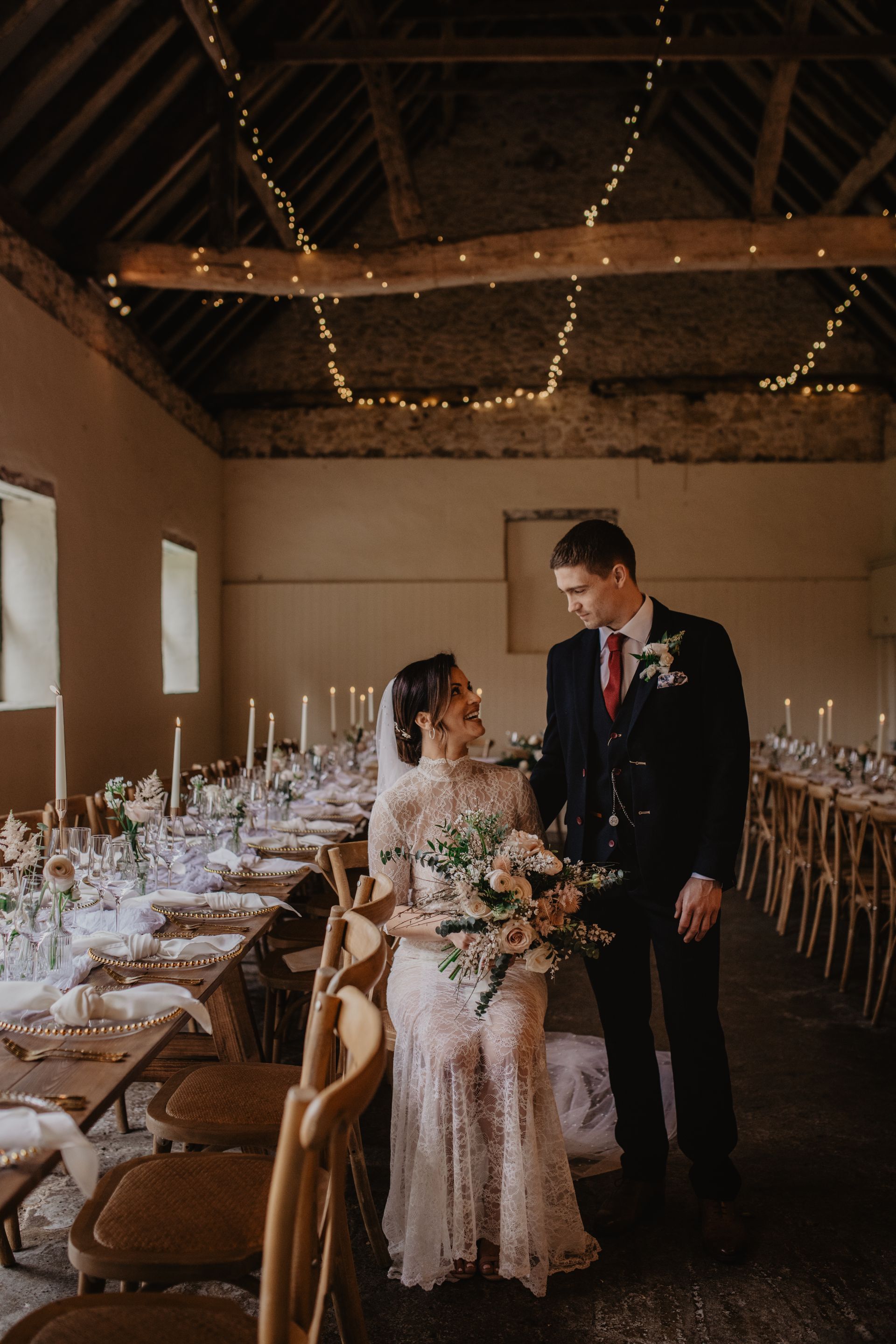 A bride and groom are standing in a room with tables and chairs.