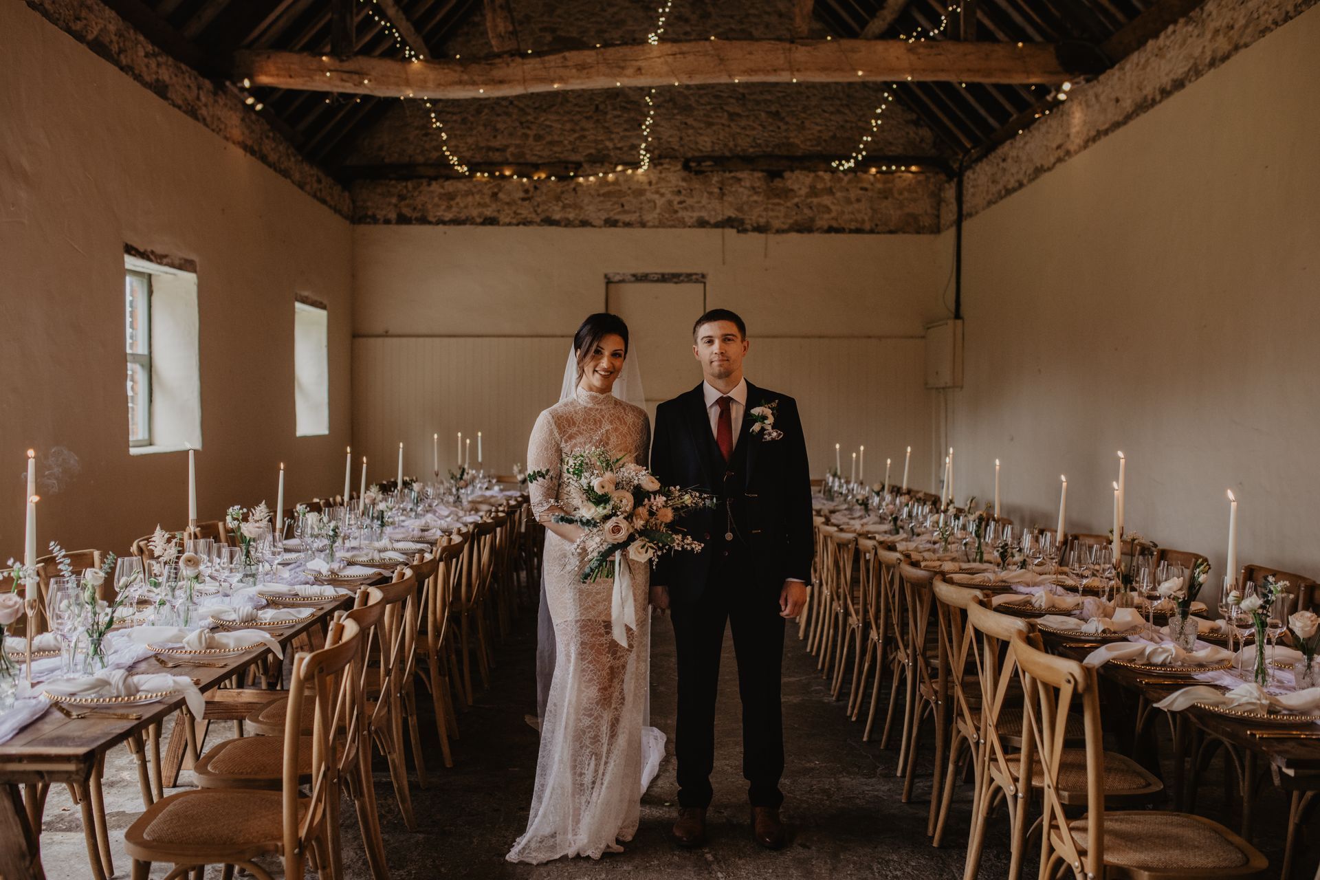 A bride and groom are standing in front of a long table.