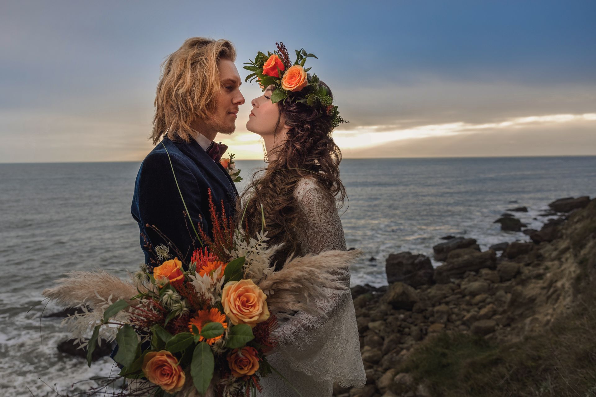 A bride and groom are standing on a rocky cliff overlooking the ocean.