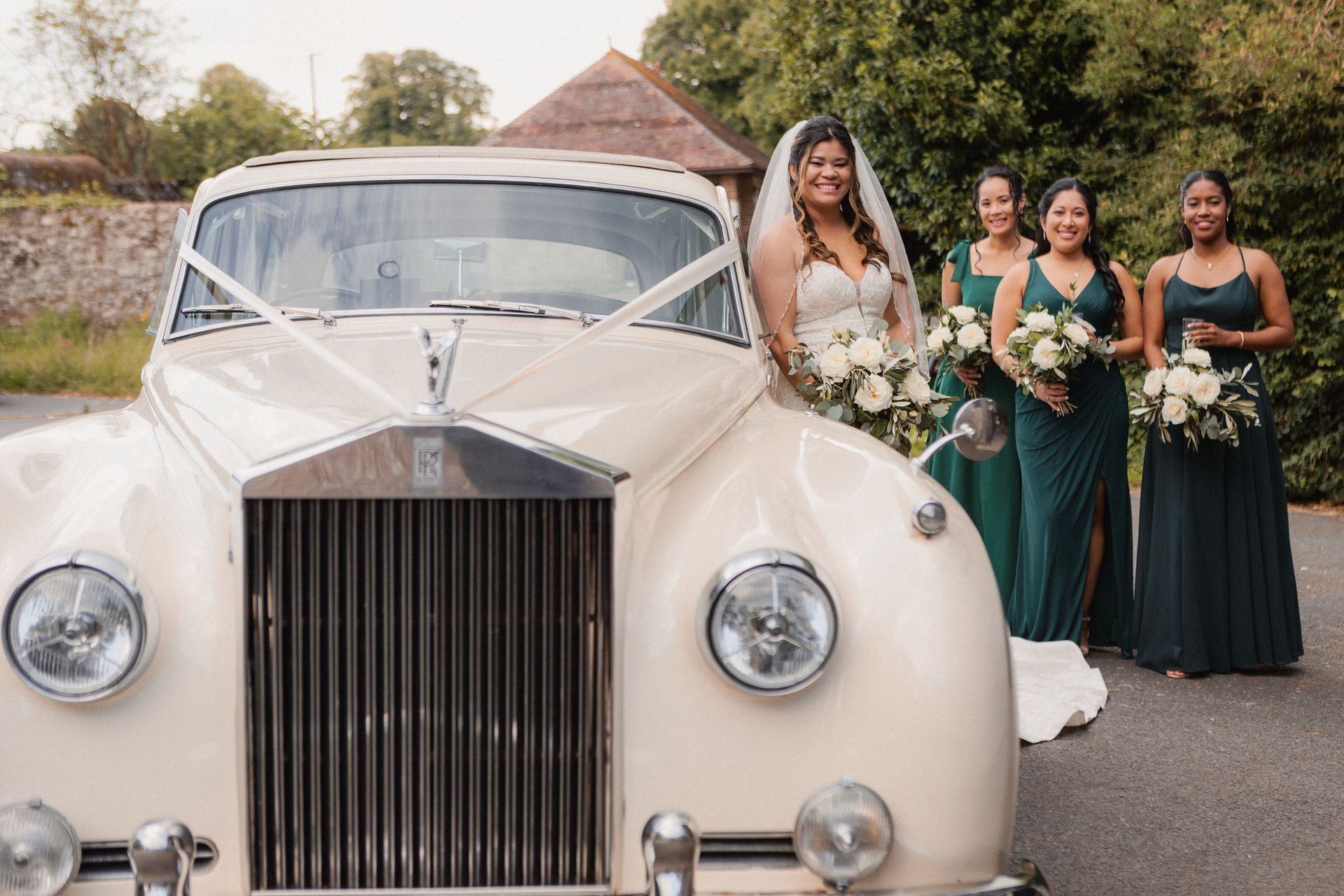 A bride and her bridesmaids are posing for a picture in front of a white rolls royce.