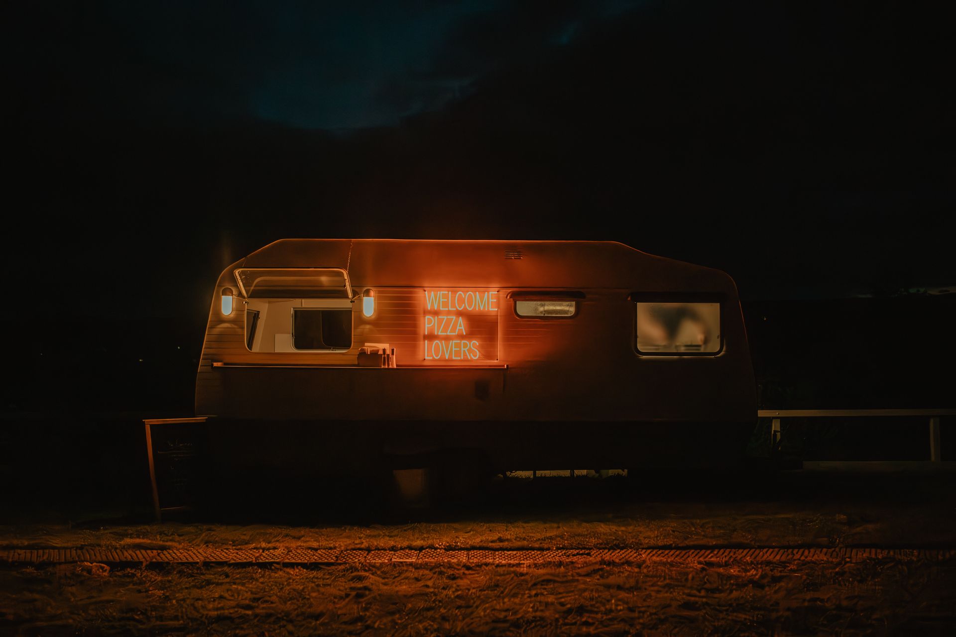 A camper trailer is lit up at night in a field.