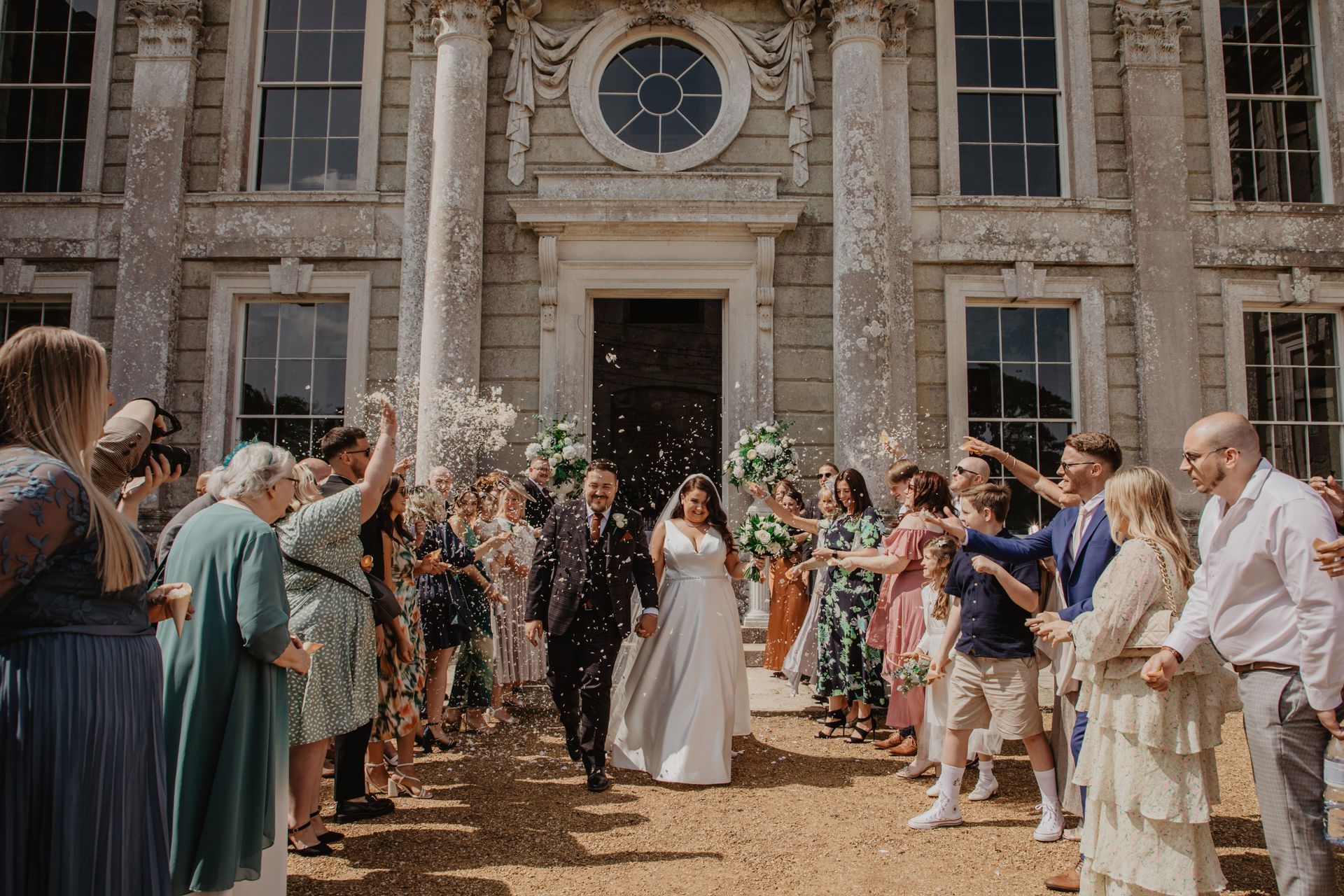 A bride and groom are being showered with confetti by their wedding guests.