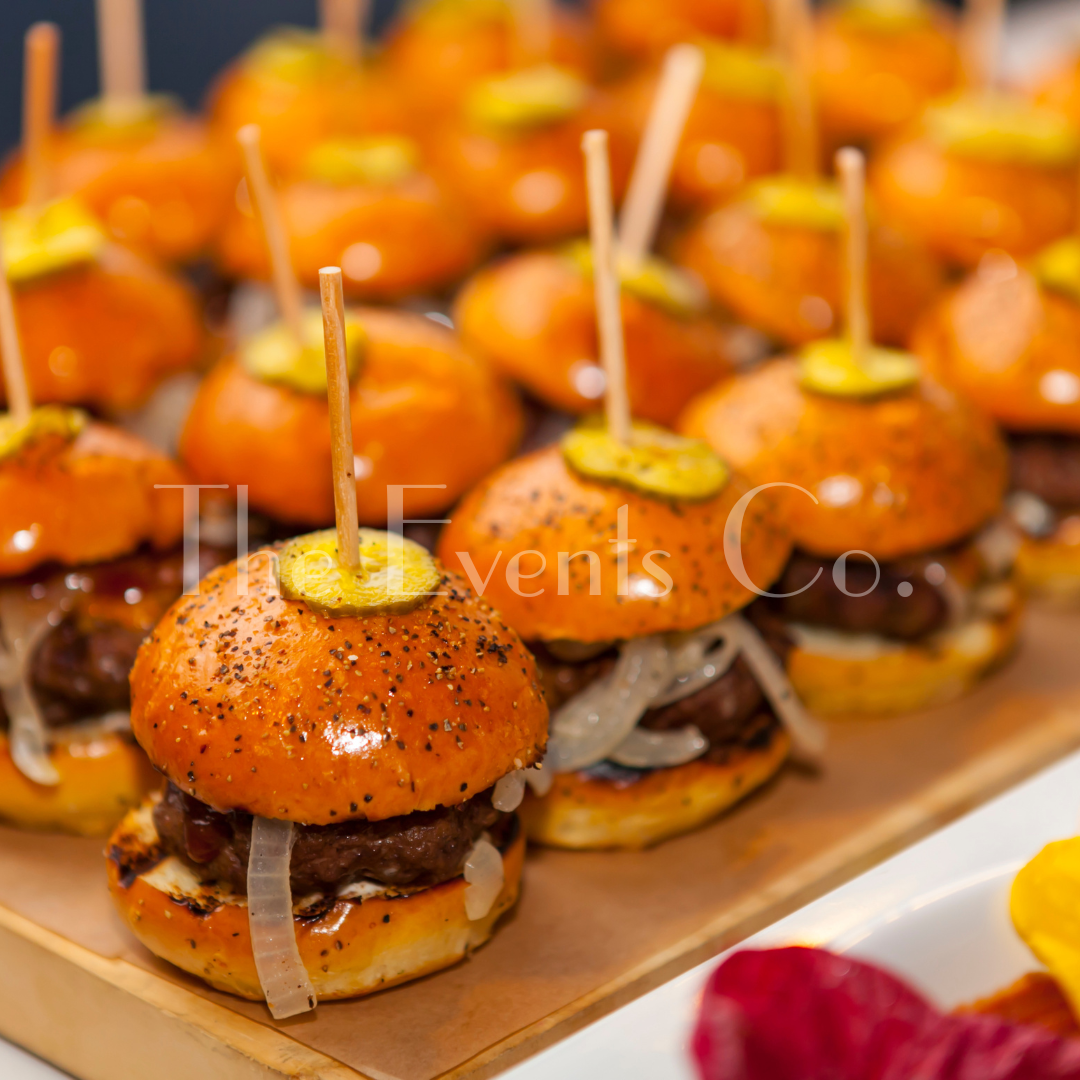 A bunch of hamburgers with pickles on top of them