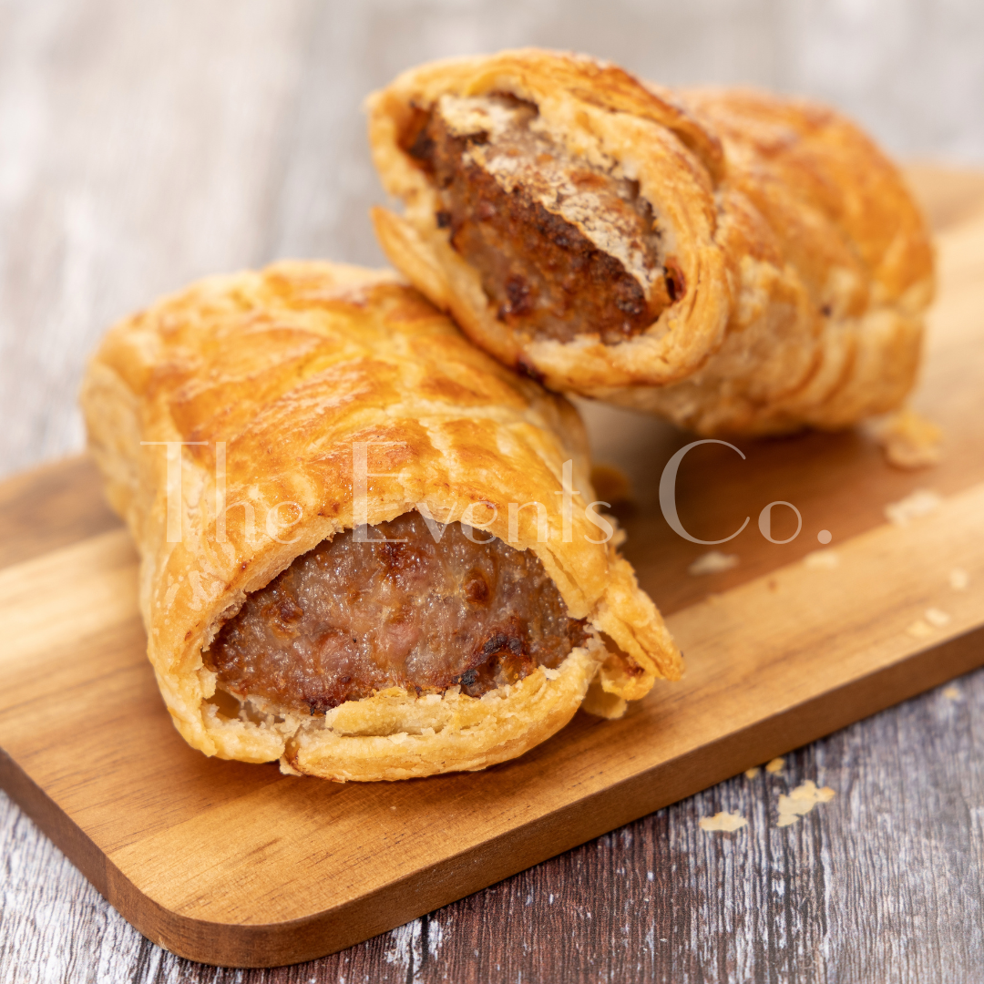 Two sausage rolls are sitting on a wooden cutting board.