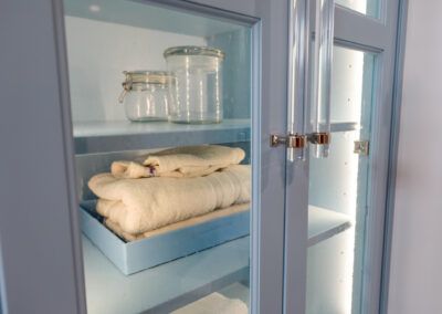 A blue cabinet with glass doors and shelves filled with towels and jars.