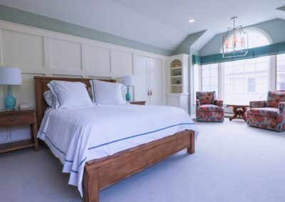 A bedroom with a bed , chairs , lamps and a large window.