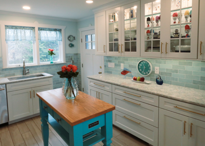 A kitchen with white cabinets and a blue island with a vase of flowers on it.