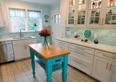 A kitchen with white cabinets and a blue island with a vase of flowers on it.