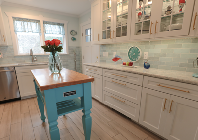 A kitchen with white cabinets and a blue island with a vase of flowers on it.