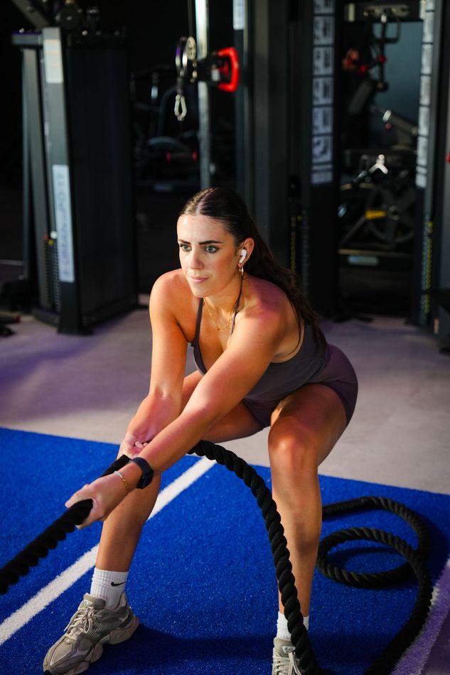 Een vrouw in een blauw crop top zwaait met een blauwe kettlebell in de sportschool.