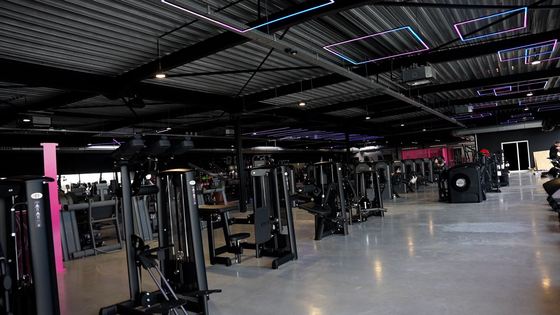 Interieur van een sportschool met rijen fitnessapparaten en een getextureerd plafond.