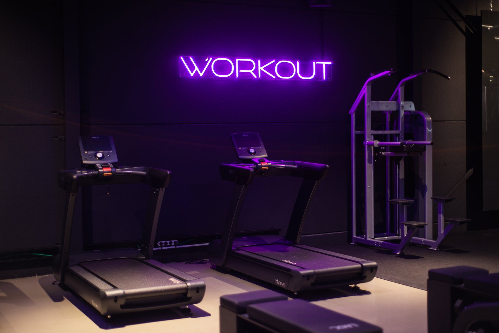 Een sportschool met loopbanden en een neonbord met de tekst 'workout'.
