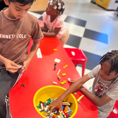 Children playing with colorful blocks around a red table and yellow bin in a play area